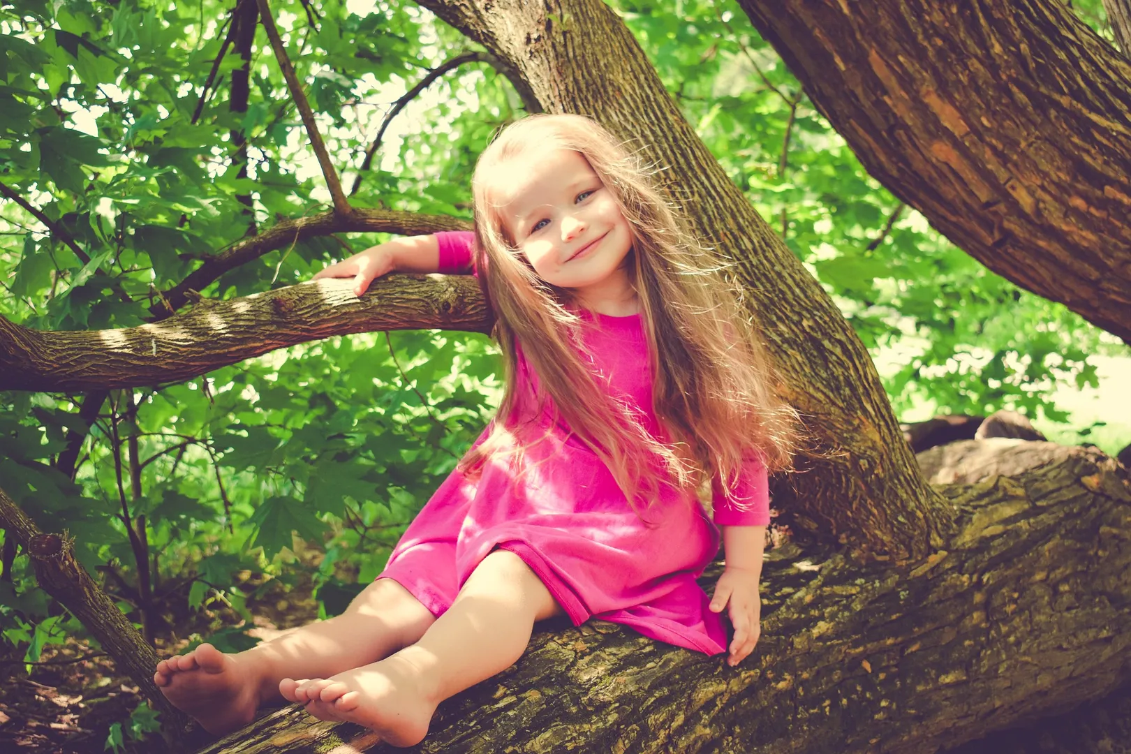 Girl smiling while sitting on tree branch.