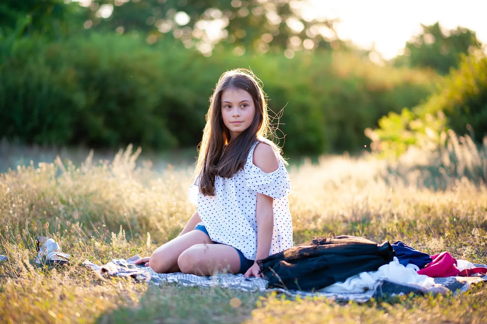 Girl sitting on blanket in a sunny field.