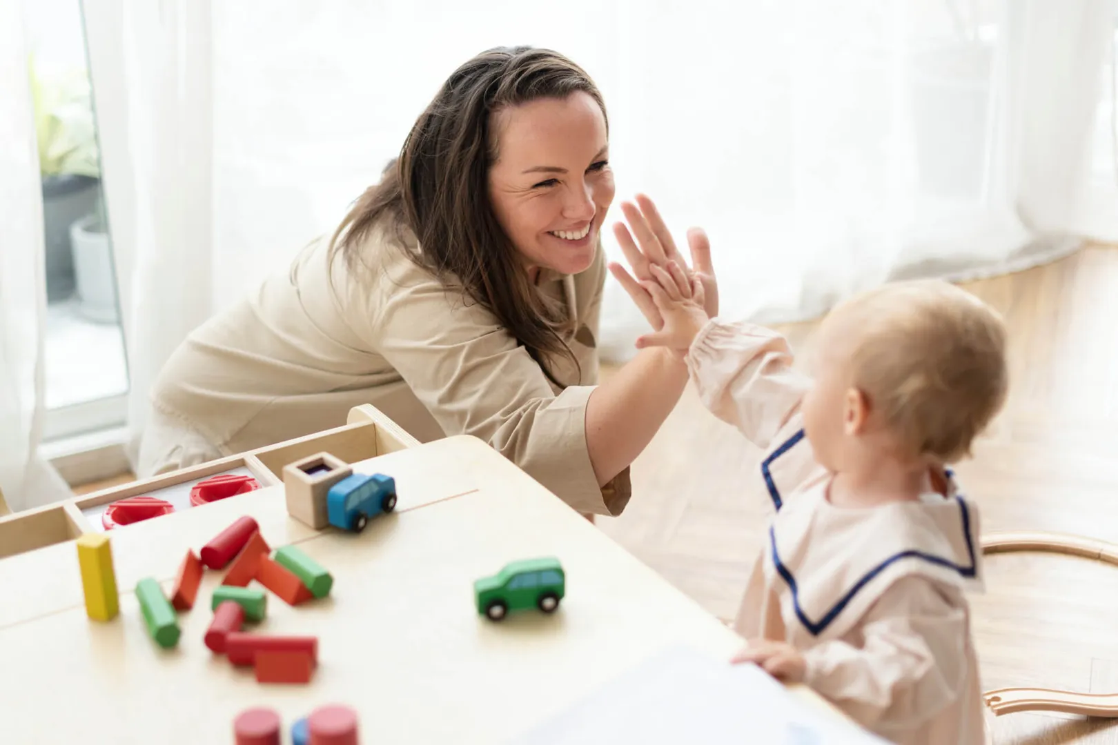 Smiling woman high-fives toddler near toy blocks.
