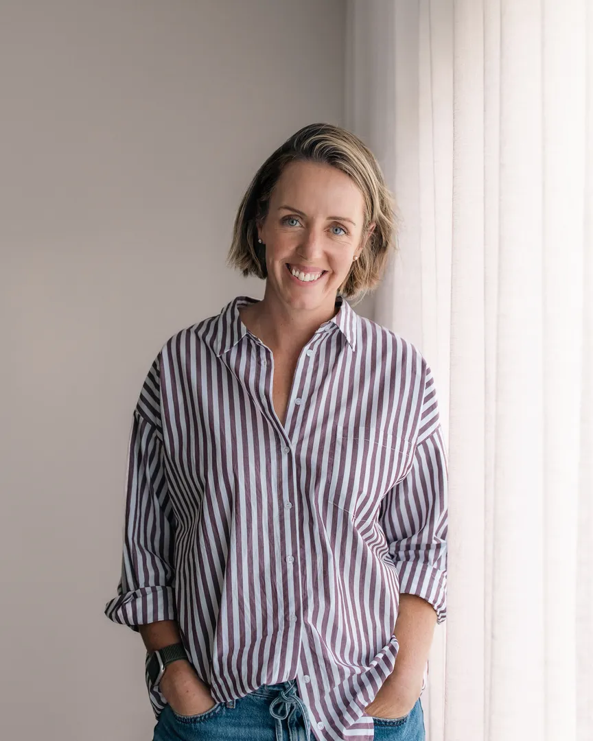 Smiling person in striped shirt near window curtains.